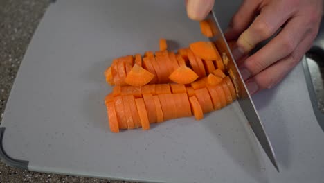 Man-hands-cutting-the-carrot-into-small-pieces-with-chefs-knife-on-grey-chopping-board-on-the-table,-top-view