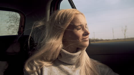 Young-blonde-woman-smiles-out-car-window-as-wind-blows-hair,-slow-motion