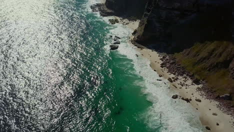 Aerial-tilt-up-revealing-rugged-ocean-coastline-and-small-sandy-beaches