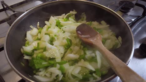 Steamy-Onion-and-Green-Pepper-in-Pan-with-Wooden-Spoon,-Slowmo-Moving-Closer