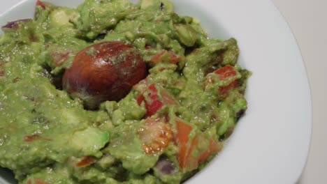 Guacamole-with-Avocado-Pit,-Closeup-Pan-Right-on-Isolated-White-Background