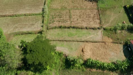 Vista-Aérea-Rápida-Sobre-Las-Tierras-De-Cultivo-En-Transición-Hacia-Un-Pueblo-Moderno-Y-Montañas-Cubiertas-De-Bosques-En-Filipinas-En-4k