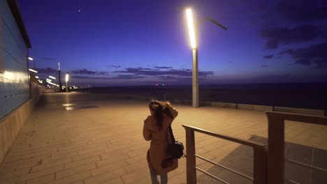 Woman-walking-along-the-promenade-on-the-beach-at-dusk-in-slow-motion