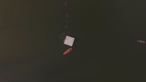 Aerial-view-of-kids-having-fun-swimming-to-a-lake's-platform-in-a-summer-camp,-with-a-kayak-and-canoe-floating-in-the-lake