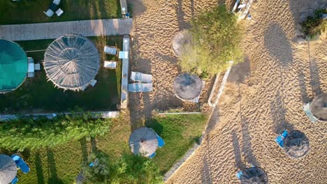 Vista-Impresionante-De-Drones-Volando-Sobre-Las-Chozas-En-La-Playa-De-Arena-Y-Resort-En-Un-Día-Soleado