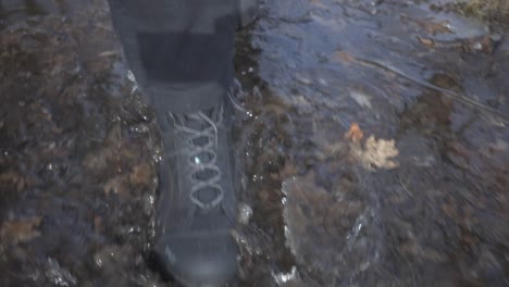 A-Person-Wearing-A-Black-Boots-Stepping-Into-The-Watery-Ground-With-Fallen-Leaves