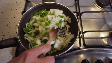Hand-stirs-green-pepper-and-onion-in-small-frying-pan,-Slowmo-Closeup