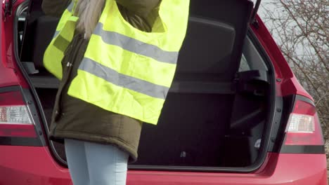 Woman-takes-out-and-puts-on-yellow-reflective-safety-vest-from-car
