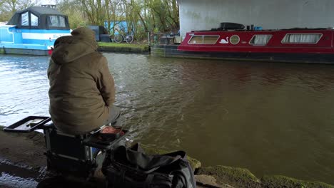 Unrecognisable-lonely-man-fishing-a-canal-under-a-bridge