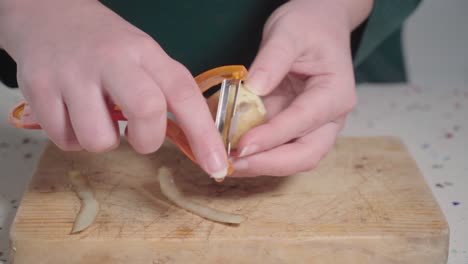 Woman-peeling-skin-of-small-potato-over-wooden-cutting-board,-Closeup