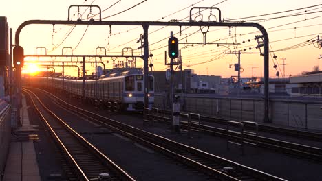Train-Driving-On-Tracks-Approaching-The-Station-In-Japan-With-Beautiful-Sunset-On-Then-Background---wide-shot
