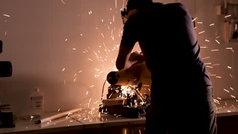 Man-in-dark-room-cuts-with-electric-saw,-sparks-flying-out,-medium-shot-pull-back