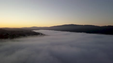 Misty-mountain-Valley-filled-with-fog-clouds-during-sunrise-with-golden-gradient-sky-camera-turning-right