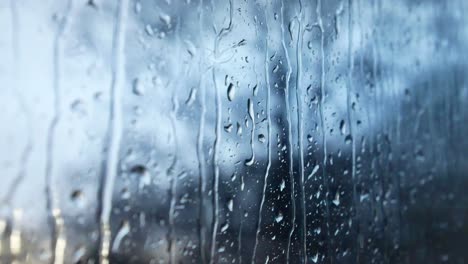 Rainy-storm-droplets,-moody-weather-fall-down-window-glass-closeup-bokeh