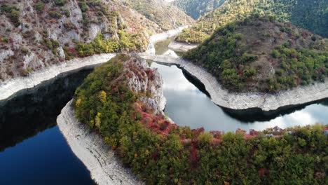 Drone-pull-away-shot-of-dark-blue-river-and-beautiful-foliage,-kanyon-Uvac,-Serbia,-slow-motion