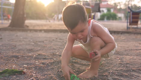 Zeitlupenvideo-Eines-Niedlichen-Asiatischen-Kindes,-Das-Glücklich-Allein-Mit-Spielzeugautos-Und-Dreck-Auf-Einem-Kinderspielplatz-Im-Freien-Bei-Sonnenuntergang-Mit-Schönem-Gegenlicht-Spielt