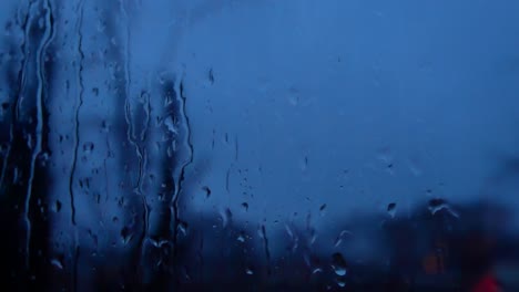 Rainy-storm-droplets-at-night,-moody-weather-fall-down-window-glass-flashing-emergency-lights-closeup-bokeh