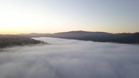 Misty-mountain-Valley-filled-with-fog-clouds-during-sunrise-with-golden-gradient-sky-camera-turning-left-slow