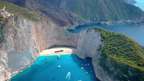 Breathtaking-aerial-view-of-crystal-clear-blue-water-of-Navagio-beach,-surrounded-by-huge-cliffs-and-mountains,-Zakynthos,-Greece