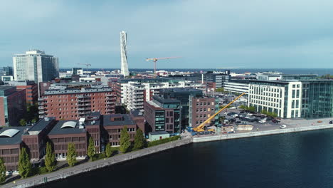 Drone-aerial-shot-of-cityscape-Turning-Torso-building-skyscraper-in-Malmö-Sweden-harbor-at-a-construction-building-site-near-the-seaside-water-with-a-large-crane-moving-pieces-of-wood-building-blocks