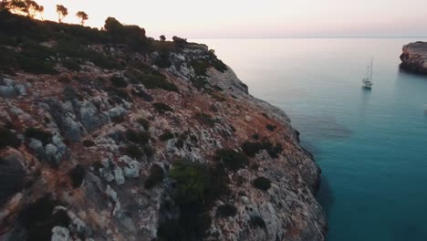 Luftaufnahmen-Eines-Sonnenaufgangs-In-Einer-Leeren-Bucht-Mit-Segelbooten-Im-Ruhigen-Mittelmeer-Auf-Mallorca,-Spanien