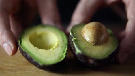 Hands-of-caucasian-male-pushing-halved-green-avocado-towards-the-camera-on-wooden-chopping-board