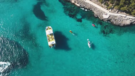 4k-aerial-footage-of-tourists-on-a-boat-in-a-tropical-bay-in-Mallorca,-Spain---Balearic-Islands