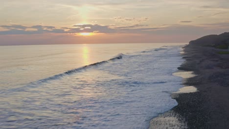 Amazing-sunset-over-beach-shoreline,-waves-crashing-against-pebble-beach,-aerial