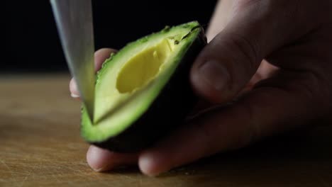 Slicing-through-green-avocado-with-tip-of-sharp-chefs-knife,-SLOW-MOTION