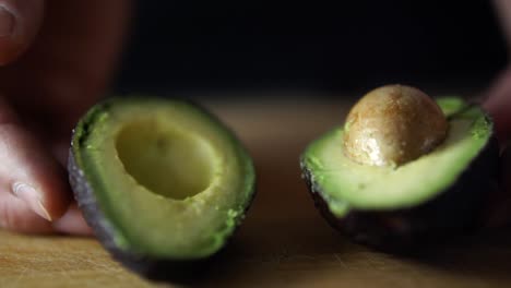 Hands-of-caucasian-male-opening-green-avocado-cut-in-half-on-wooden-chopping-board,-SLOW-MOTION