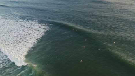 Aerial:-beautiful-perfect-wave-motion,-surfers-waiting-on-boards-in-sea