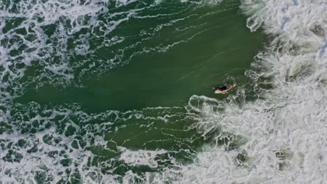 Aerial:-surfer-duck-diving-technique-under-large-breaking-wave,-bird's-eye-view