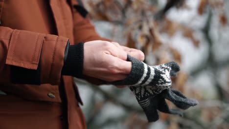 Man-putting-gray-cotton-glove-with-white-patterns-on-his-hand-in-forest-on-cold-winter-day,-SLOW-MOTION
