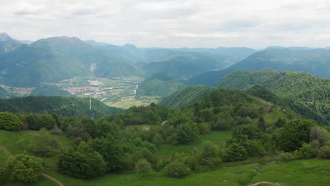 Aerial-view-of-Tolmin-basin-from-mountain-Kolovrat,-Soca-river-and-fileds-visible,-lots-of-greenery-and-trees,-cloudy-skies-in-summer