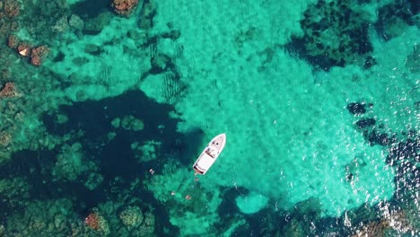 Aerial-top-down-shot-in-4k-of-people-swimming-next-to-a-yacht-in-crystal-clear-blue-and-turquoise-Mediterranean-Sea-in-Mallorca,-Spain---Luxury-Holiday---Balearic-Islands
