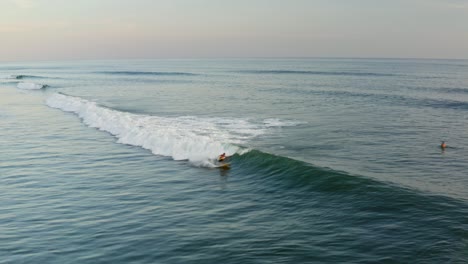 Wunderschönes-Surfziel,-Surfer,-Die-Bei-Sonnenuntergang-Am-Tropischen-Strand-Wellen-Reiten