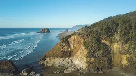 Stunning-aerial-footage-of-the-westcoast-landscape-in-Oregon---Lion-rock-near-cannon-beach---large-empty-beach-with-beautiful-green-forest-and-huge-trees