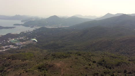 Paragliding-over-Hong-Kong-mountains-on-a-beautiful-clear-day-with-Skyscrapers-in-the-horizon,-Aerial-footage