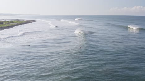 Aerial:-surfers-relaxing-on-surfboards-behind-perfectly-breaking-waves,-remote-Mexican-surf