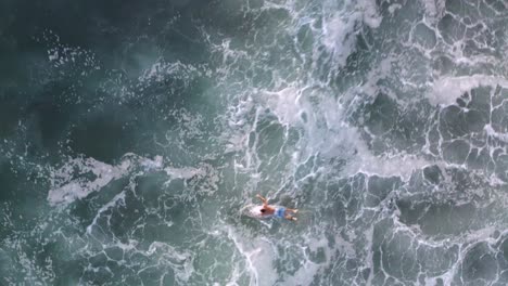 Aerial:-amazing-footage-of-surfer-paddling-through-strong-ocean-waves,-bird's-eye-view
