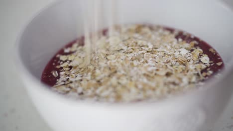 Sprinkling-oats-on-top-of-red-berry-smoothie-in-white-ceramic-bowl