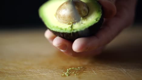Caucasian-male-hand-holding-halved-avocado-and-taking-out-its-pit-with-sharp-chefs-knife,-SLOW-MOTION