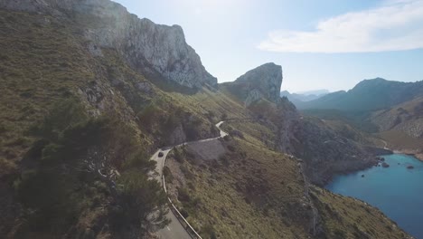 4k-aerial-footage-of-a-car-driving-on-a-serpentine-road-next-to-a-cliff-in-the-massive-mountain-line-Serra-de-Tramuntana-in-Mallorca,-Spain