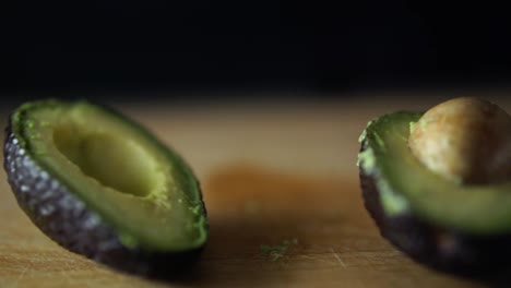 Fingers-of-caucasian-male-releasing-halved-avocado-which-is-being-split-open-on-wooden-chopping-board,-SLOW-MOTION