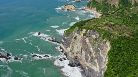 Aerial:-waves-crashing-against-rugged-cliffs-on-Pacific-Coast,-high-reveal