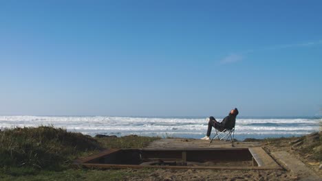 Mann-Sitzt-Im-Klappstuhl-Am-Strand-Und-Beobachtet-Die-Wellen-Im-Ozean-Und-Denkt-über-Das-Leben-Nach---Erholsamer-Urlaub---Freiheit---Allein-Und-D-Introvertiert,-4k-Aufnahmen-In-Zeitlupe