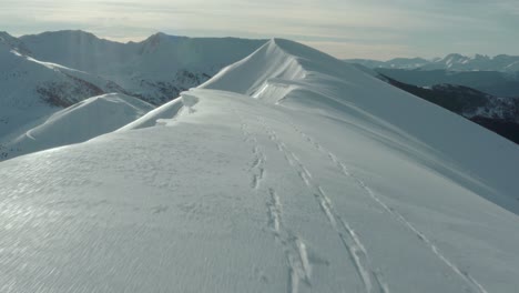 Aerial:-ski-tracks-in-snow-on-mountain-peak-ridge,-nature-summit-reveal