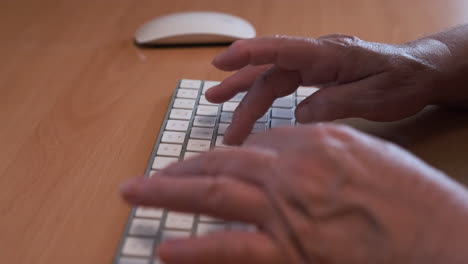 Hände-Einer-älteren-Frau,-Die-Auf-Einer-Weißen-Computertastatur-Auf-Dem-Schreibtisch-Tippt