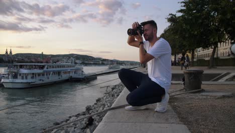 4k-footage-of-young-man-taking-pictures-while-sunset-with-professional-dslr-camera-next-to-the-Donau-river-in-Budapest-Hungary