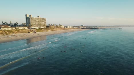Fantastische-Vogelperspektive-Auf-Den-Pazifischen-Strand-Und-Den-Kristallpier-Von-San-Diego---4k-drohnenaufnahme---Surfen-Bei-Sonnenuntergang